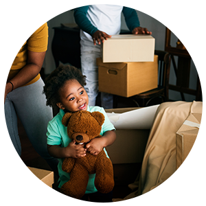 a small child holding a teddy bear with unpacked boxes around